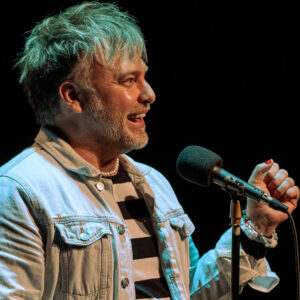 Steven Burge speaking into a microphone at The Narrators in Denver, Colorado